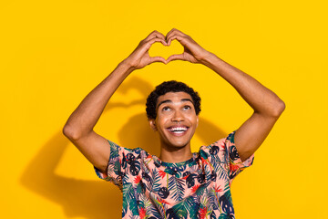 Photo of young smiling man support donation blood for ill people showing love symbol looking above isolated on yellow color background