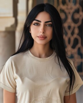 A young Arabic woman with black hair wearing a beige shirt poses, facing the camera