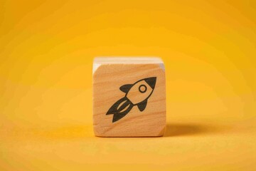 Wooden block with rocket printed on it, startup and business concept, yellow background.