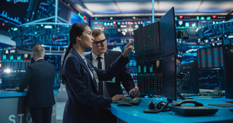 Asian Female and Male Stock Exchange Agents Using Computer, Discussing Investment Strategy for an International Business Client, Working in an Office Building Surrounded by Computer Screens