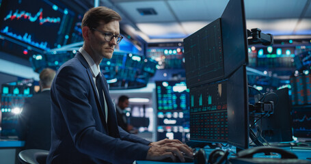 Portrait of Young Handsome Stock Exchange Broker Working on Computer, Researching Real-Time Stocks Data, Analyzing Commodities and Exchange Market Charts. Professional Investment Agent in Office - obrazy, fototapety, plakaty