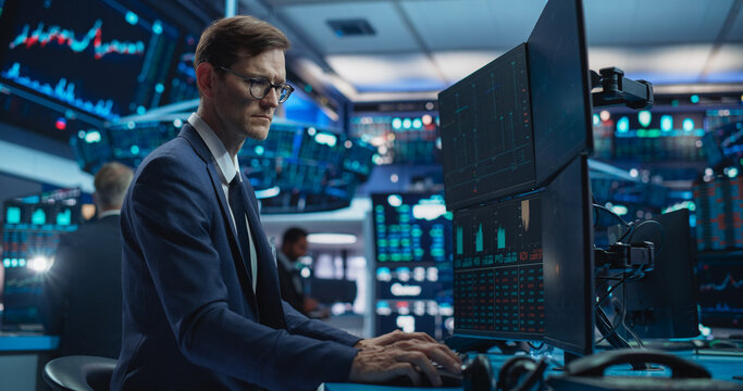 Portrait of Young Handsome Stock Exchange Broker Working on Computer, Researching Real-Time Stocks Data, Analyzing Commodities and Exchange Market Charts. Professional Investment Agent in Office