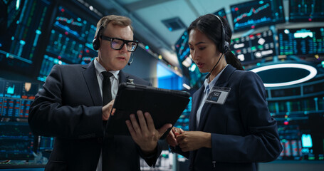 Two Successful Stock Exchange Traders Using Tablet Computer, Discussing Commodities Investments for an International Business Partner, Working in a Modern Office with Multiple Computer Screens