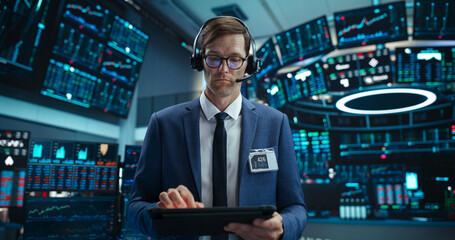 Portrait of a Young Handsome Stock Exchange Broker Using Tablet Computer, Researching Real-Time Stocks Data, Analyzing Commodities and Exchange Market Charts. Professional Investment Agent in Office