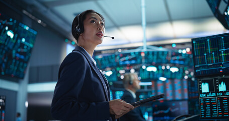 Successful Stock Exchange Manager Wearing Headphones, Working in Modern Office. Proactive Female Trader Browsing Financial Reports on a Tablet Computer, Using Software with Stock Market Auctions