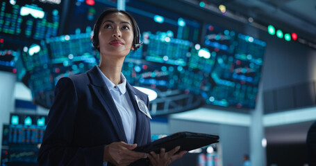 Female Investment Banker Wearing Headphones and Using a Tablet Computer with Financial Market Analytics Data. Team Leader Monitoring Daily Operations, Working of Behalf of Corporate Business Partners