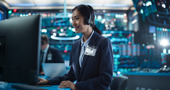 Female Stock Exchange Banker Working on a Desktop Computer with Real-Time Stocks, Commodities and Securities Market Charts. Professional Asian Investor Talking on a Mic with Business Partners - Powered by Adobe
