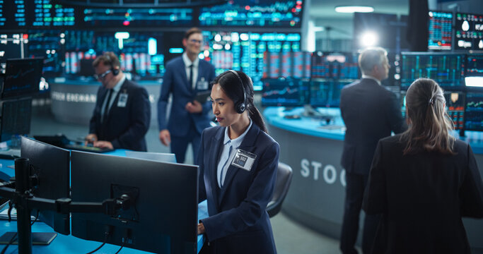 Female Stock Exchange Banker Working on a Desktop Computer with Real-Time Stocks, Commodities and Securities Market Charts. Professional Asian Investor Talking on a Mic with Business Partners