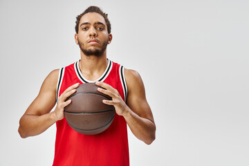 good looking african american man in sportwear holding basketball and looking straight at camera