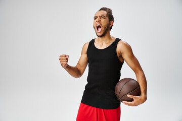 good looking emotional african american man in sport attire posing with basketball on gray backdrop