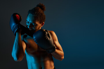 handsome shirtless african american man in sport shorts wearing boxing gloves surrounded by lights