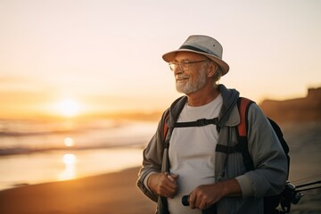 Senior man with a backpack on the beach at sunset. Portrait of an elderly man with a backpack.