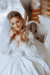 Fototapeta na wymiar fashion photo of a beautiful bride with dark hair in an elegant wedding dress and stunning makeup in the room on the morning of the wedding. The bride is preparing for the wedding