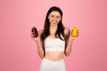 Happy young woman in a white sports top holding two bottles of colorful detox juice