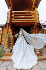 A blonde bride in a voluminous white dress holds a bouquet, poses. The veil is thrown into the air. Beautiful hair and makeup. Wedding photo session in nature. Long train of the dress