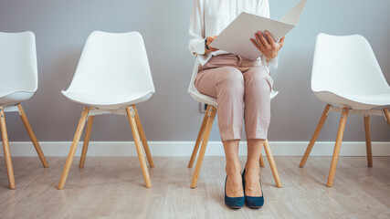 Studio shot of a young businesswoman using a laptop while waiting in line against a gray background. Young woman sitting in lobby with resume in hands and waiting for job interview