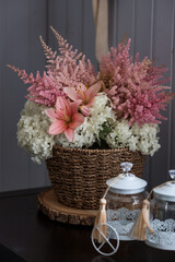 A beautiful, delicate bouquet of pink lilies, white hydrangea and pink astilbe in a wicker basket in the interior. Close-up. Decor.