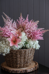 A beautiful, delicate bouquet of pink lilies, white hydrangea and pink astilbe in a wicker basket in the interior. Close-up. Decor.