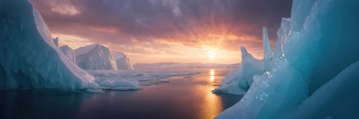 Rolgordijnen sun sets behind a cluster of towering icebergs, casting a warm orange glow across the icy landscape. The icebergs are majestically floating in the calm waters, creating © petrovk