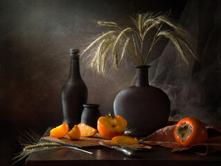 Autumn still life with persimmon and rye in a black bottle on a dark background