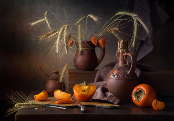 Autumn still life with persimmons and rye in a clay jug on a dark background