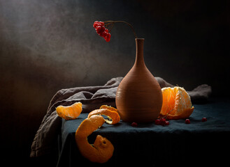 Modern still life with a tangerine and a viburnum branch in a clay vase on a dark background