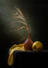 Modern still life with quince and a dry branch in a clay vase on a dark background