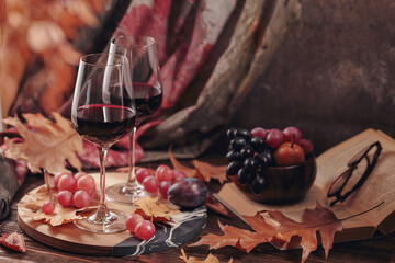 Autumn still life with two glasses of red wine, grapes, book and dry leaves in rustic style on dark...
