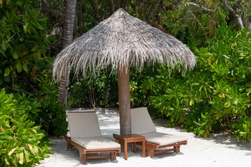 Sun loungers under a thatched umbrella on a beach in the Maldive Islands