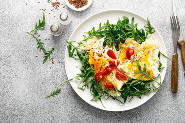 Fried eggs, omelette with onions, tomatoes and fresh arugula salad, top view