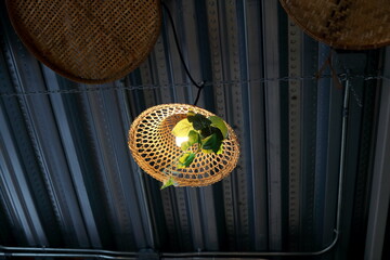 Bamboo native Thai style weaving cover lamp hanging under dark gray wave shape metal ceiling, Thailand.