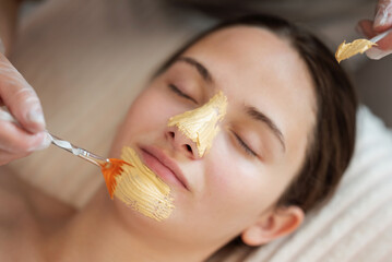 Close up of young girl`s face with closed eyes, cosmetologist applies facial mask on her skin....
