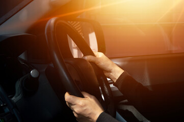 Man driving car, hand on steering wheel, looking at the road ahead,sunset.