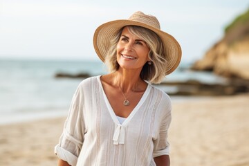 smiling mature woman in hat and white blouse standing on beach