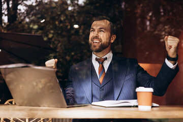 Business man sitting in a cafe behind window working on laptop and drinking coffee