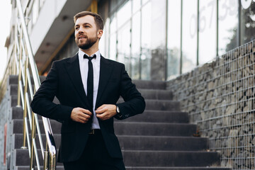 Handsome business man in black suit walking down the stairs by office center