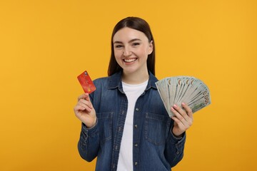 Happy woman with credit card and dollar banknotes on orange background
