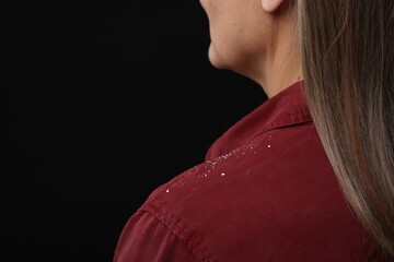 Woman with dandruff on her shirt against black background, closeup. Space for text