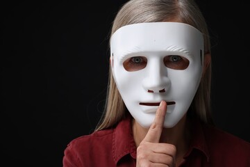 Multiple personality concept. Woman in mask showing hush gesture on black background, space for text