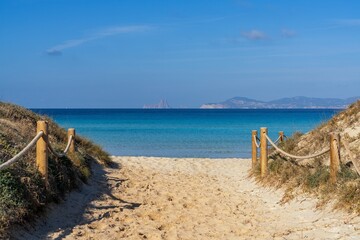 beach access leads to Ses Illetes beach on Formentera with a view of Ibiza and Es Vedra in the background