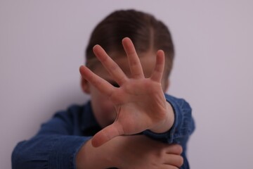 Child abuse. Girl making stop gesture near grey wall, selective focus