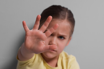 Child abuse. Girl making stop gesture near grey wall, selective focus
