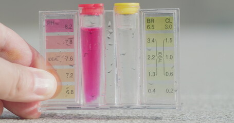 A hand holds a test tube with tests for PH and chlorine levels.