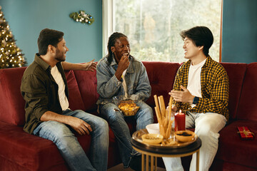 Cheerful young people eating snacks and talking while having Christmas home party together