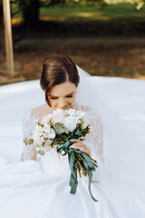 The brunette bride, smiling sincerely, sits on the ground in her unfolded dress and holds a...