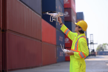 An engineer or worker uses a remote control to control a drone at a container port to inspect...