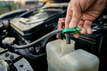 Close-up of an auto mechanic's hand opening the coolant tank cap, checking the coolant level in the...