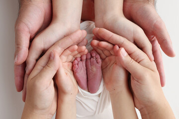The palms of the father, the mother are holding the foot of the newborn baby in a white blanket. Feet of the newborn on the palms of the parents. Studio macro photo of a child's toes, heels and feet.