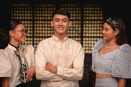 Three cheerful young individuals showcasing traditional Filipino clothing with a nice capiz shell window background.