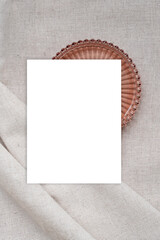 Blank white paper card mockup and decorative copper color plate on textured neutral beige linen fabric surface